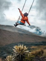 Una persona en un columpio con un paisaje montañoso al fondo.