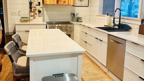 Una cocina moderna con armarios blancos, una isla central, electrodomésticos de acero inoxidable y un ventilador de techo.