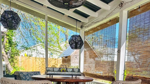 Un espacio al aire libre techado con sillas de mimbre y una mesa de madera, que ofrece vistas al jardín trasero.