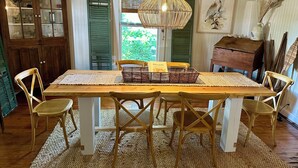 Un comedor con mesa de madera, sillas de mimbre, un mantel tejido y una lámpara colgante.