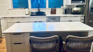 Una cocina con una isla central, dos sillas de mimbre, microondas y refrigerador.