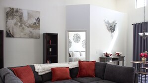 Un salon moderne avec un canapé gris, des coussins rouges, une bibliothèque, un élément décoratif mural et une petite table agrémentée de fleurs.