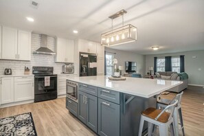 A modern kitchen with white cabinets, stainless steel appliances, and a large island. - Eco Friendly Getaway (Lowell)