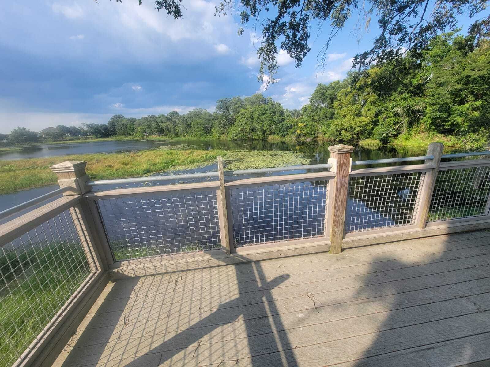 A wooden boardwalk with a metal railing overlooking a body of water and lush greenery.