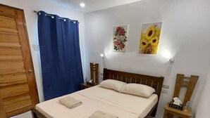 A bedroom with a wooden bed, white bedding, a blue curtain, a small bedside table with a lamp, and two wall-mounted paintings. - Room-Cola Inn (San Juan)