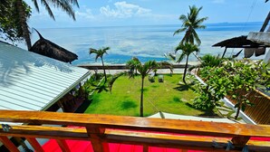 A view from a balcony overlooking a tropical beach with clear blue water, palm trees, and a small boat. - Room-Cola Inn (San Juan)