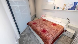 A modern bedroom with a bed, bedside table, and a shelf with books and a giraffe figurine. - River Side View Luxury Penthouse Apartment (London)
