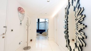 A modern hallway with a white floor, a tall floor lamp, a decorative vase, and a unique wall art piece. - River Side View Luxury Penthouse Apartment (London)
