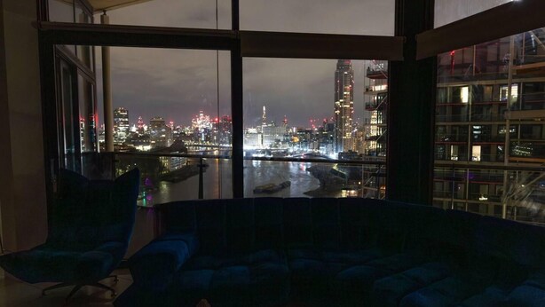 A modern living room with a large window overlooking a cityscape at night. - River Side View Luxury Penthouse Apartment (London)