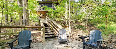 Una cabaña con terraza de madera, dos sillas Adirondack, un brasero y una escalera que lleva a la cabaña.
