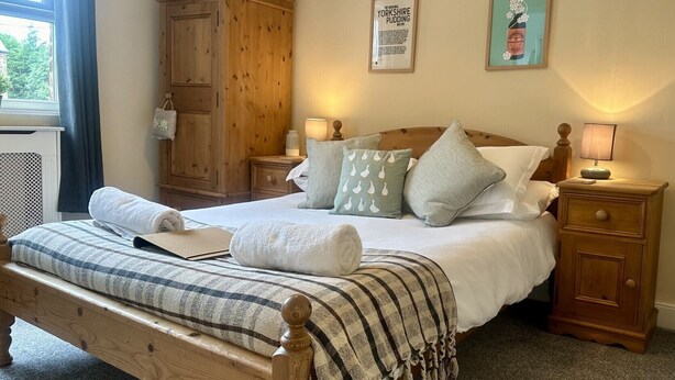 A cozy bedroom with a wooden bed, a nightstand, a wooden wardrobe, and a framed recipe on the wall. - Pinfold Cottage (York)