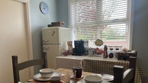 A dining area with a table set for four, a refrigerator, and a window with blinds. - Pinfold Cottage (York)