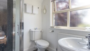 A bathroom with a toilet, a shower enclosure, a sink, and a window with frosted glass. - Pinfold Cottage (York)