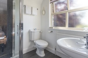 A bathroom with a toilet, a shower enclosure, a sink, and a window with frosted glass.