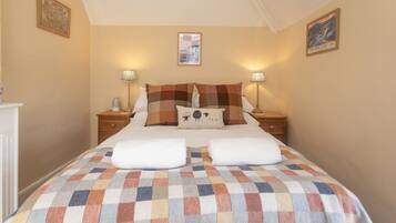 A bedroom with a checkered bedspread, two bedside tables with lamps, a cityscape mirror, and two framed pictures on the walls.