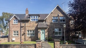 A two-story stone house with a green door, a brick exterior, and a small front garden. - Pinfold Cottage (York)