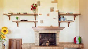 A fireplace with a brick surround, wooden shelves above, and a vase with flowers on the left.