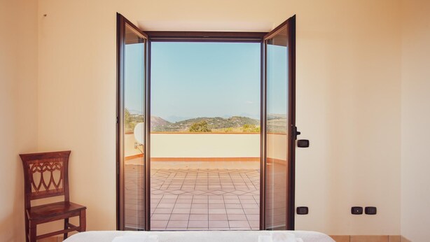 A bedroom with a large sliding glass door leading to a balcony with a view of hills.