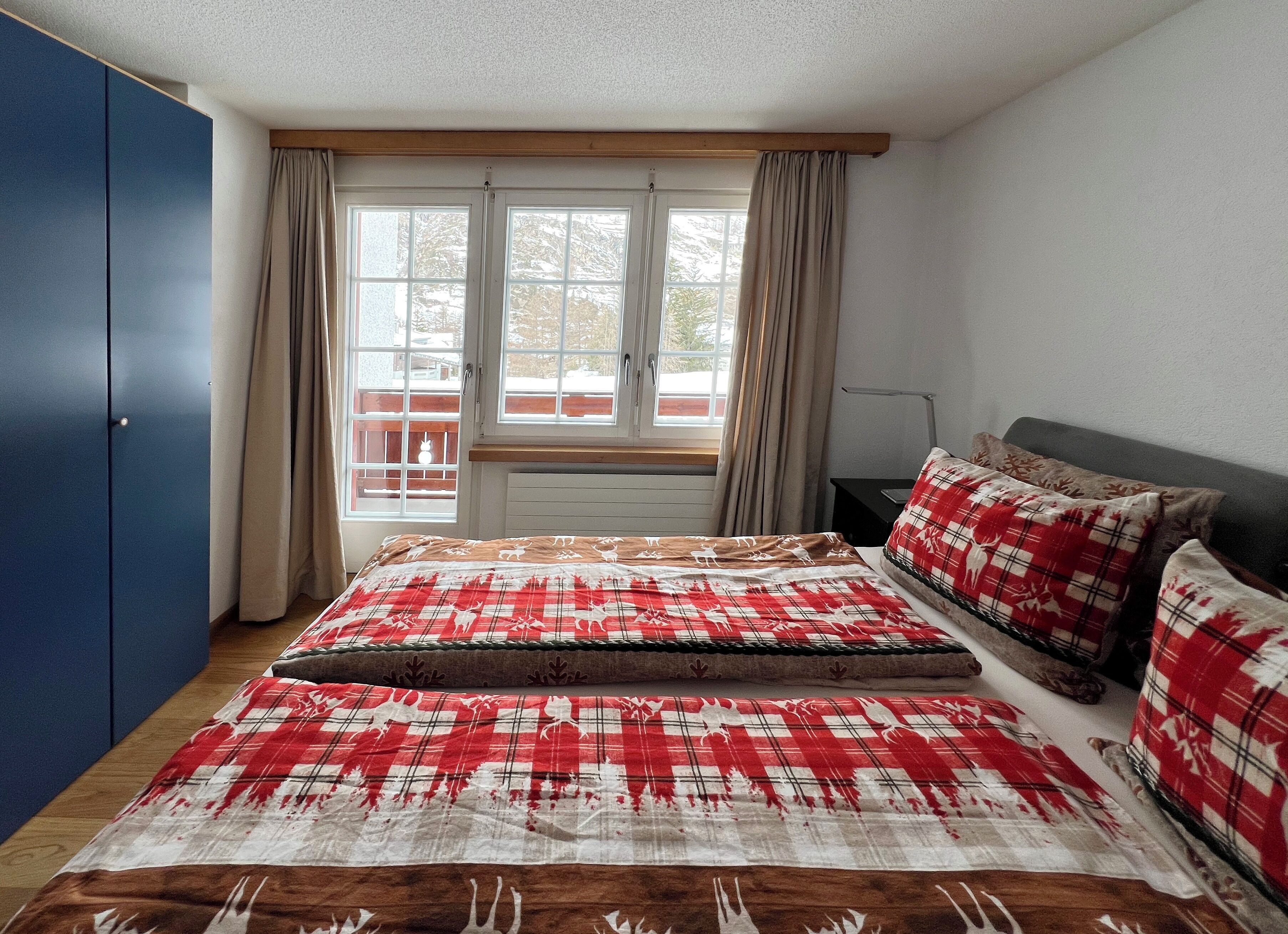 A bedroom with a large bed, a wardrobe, a window with curtains, and a view of the outside.