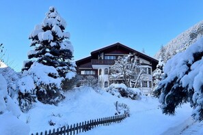 Eine schneebedeckte Lodge mit Holzfassade, umgeben von schneehohen Bäumen und einem Holzzaun.