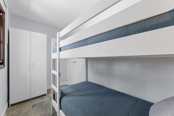 Una cama litera con colchón azul, un armario blanco y suelo de baldosas.