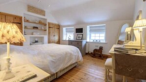 A bedroom with a bed, a desk, a chair, a lamp, a shelf with decorative items, and a window with blinds. - French Vintage Cottage in the Heart of the Fens (Spalding)