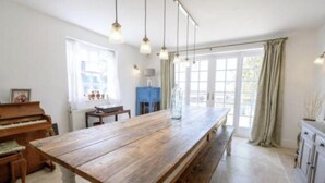 A spacious kitchen with a long wooden table, a piano, and a large window with curtains. - French Vintage Cottage in the Heart of the Fens (Spalding)