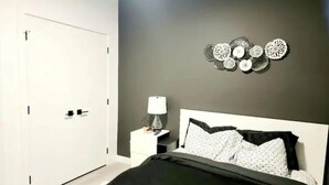A bedroom with a bed, a nightstand, a lamp, and wall decor. - Brand New Stylish Suite with separate entrance (Calgary)