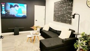 A modern living room with a black sofa, a flat-screen TV, a coffee table, and a large abstract painting on the wall. - Brand New Stylish Suite with separate entrance (Calgary)