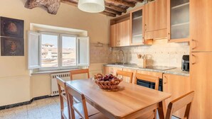 Een keuken met houten kastjes, een eettafel met stoelen, een fruitmand en een hangende lamp.