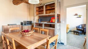 Een gezellige keuken met houten kastjes, een eettafel met stoelen, een magnetron en een mand met rode appels.