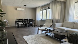 A modern living room with a sofa, coffee table, dining table with chairs, and a large window with curtains. - Modern house for 6 people - close to Gekås Ullared (Hallands län)