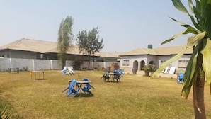 A grassy outdoor area with a table and chairs, a playground, and a building with a tiled roof. - fish eagle backpackers (Lusaka)