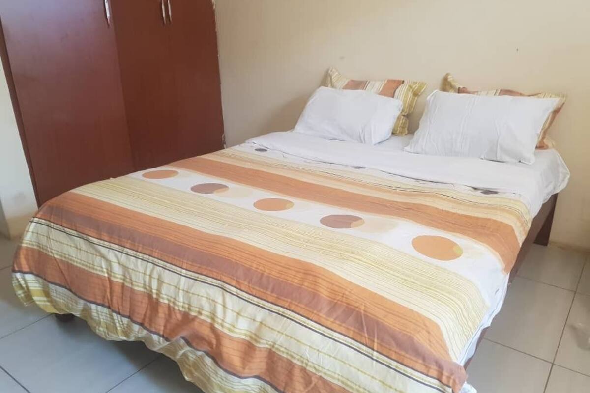 Una cama con una colcha a rayas, un armario y una pared lisa.