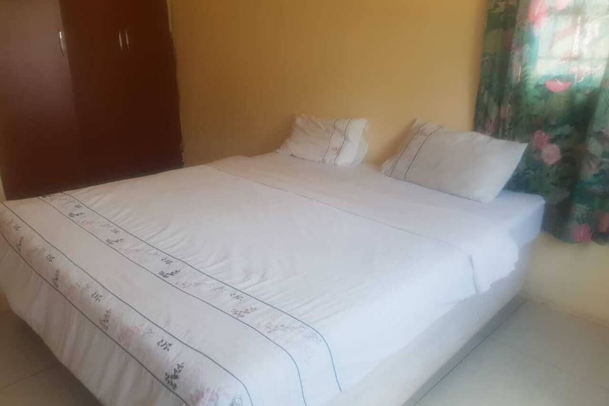 Una cama con colcha y almohadas estampadas con motivos florales, un armario de madera y una ventana con cortinas florales.