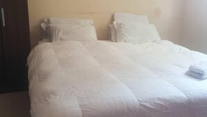 A neatly made bed with white bedding in a room with a plain wall and a wooden door. - fish eagle backpackers (Lusaka)