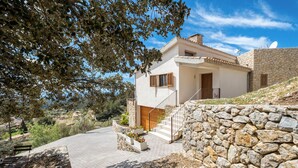 A modern house with a stone wall, a wooden staircase, and a paved driveway.