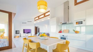 A modern kitchen with white cabinets, a microwave, and a dining area with a wooden table and yellow chairs.