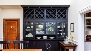 A dining area with a wooden table and chairs, a black cabinet with glass doors displaying dishes, and a wooden door. - Red House Paso- Modern Farmhouse Downtown (Paso Robles)