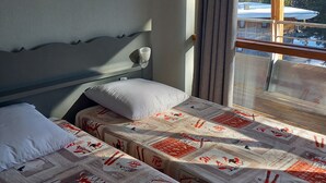 Een hotelkamer met twee bedden, elk voorzien van een bedovertrek met een patroon, een hoofdbord en een raam met uitzicht op bomen en bergen.