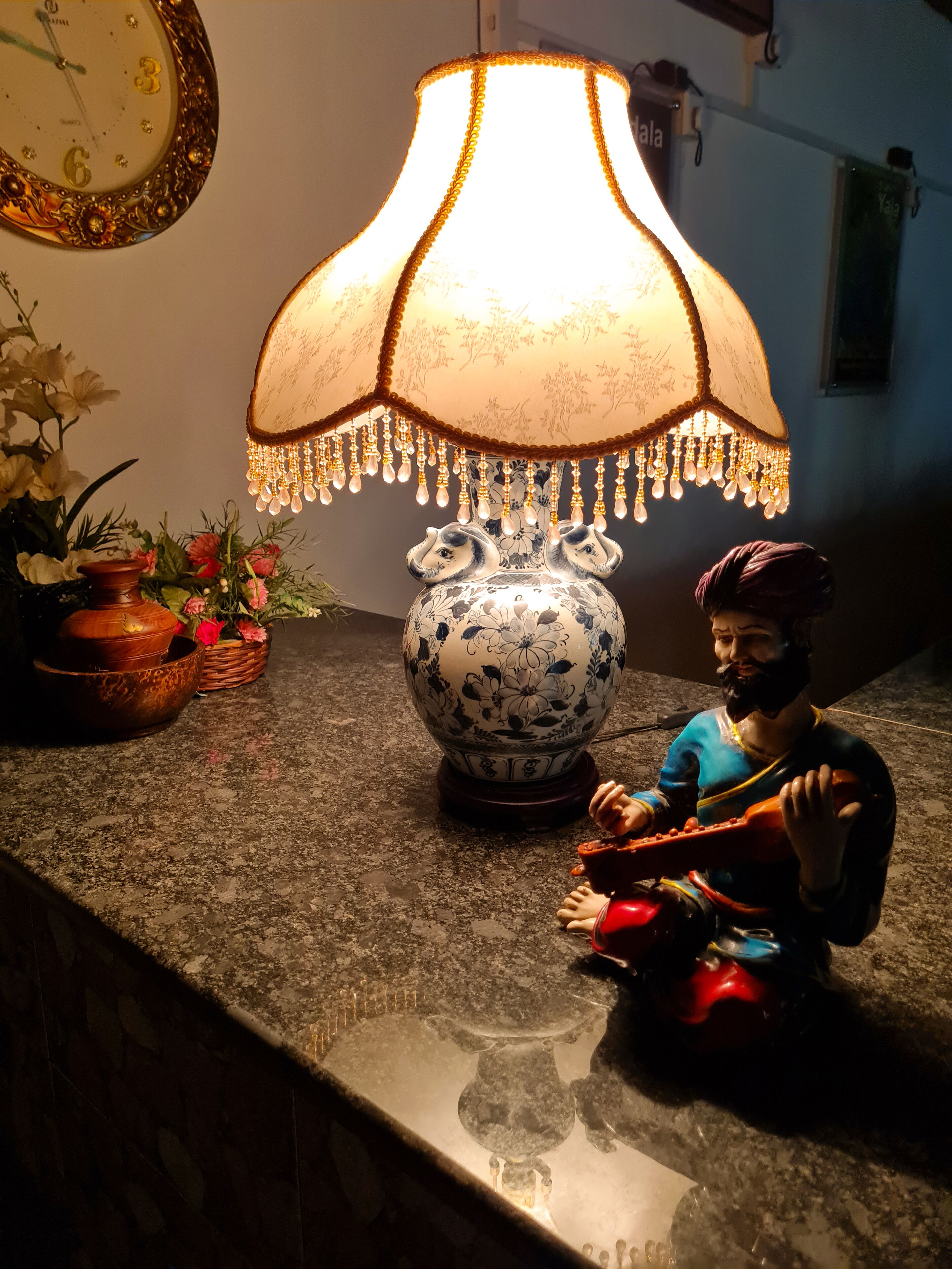Une lampe décorative ornée de motifs floraux et de pendentifs, un vase en céramique à décor floral et une petite figurine posée sur un comptoir.