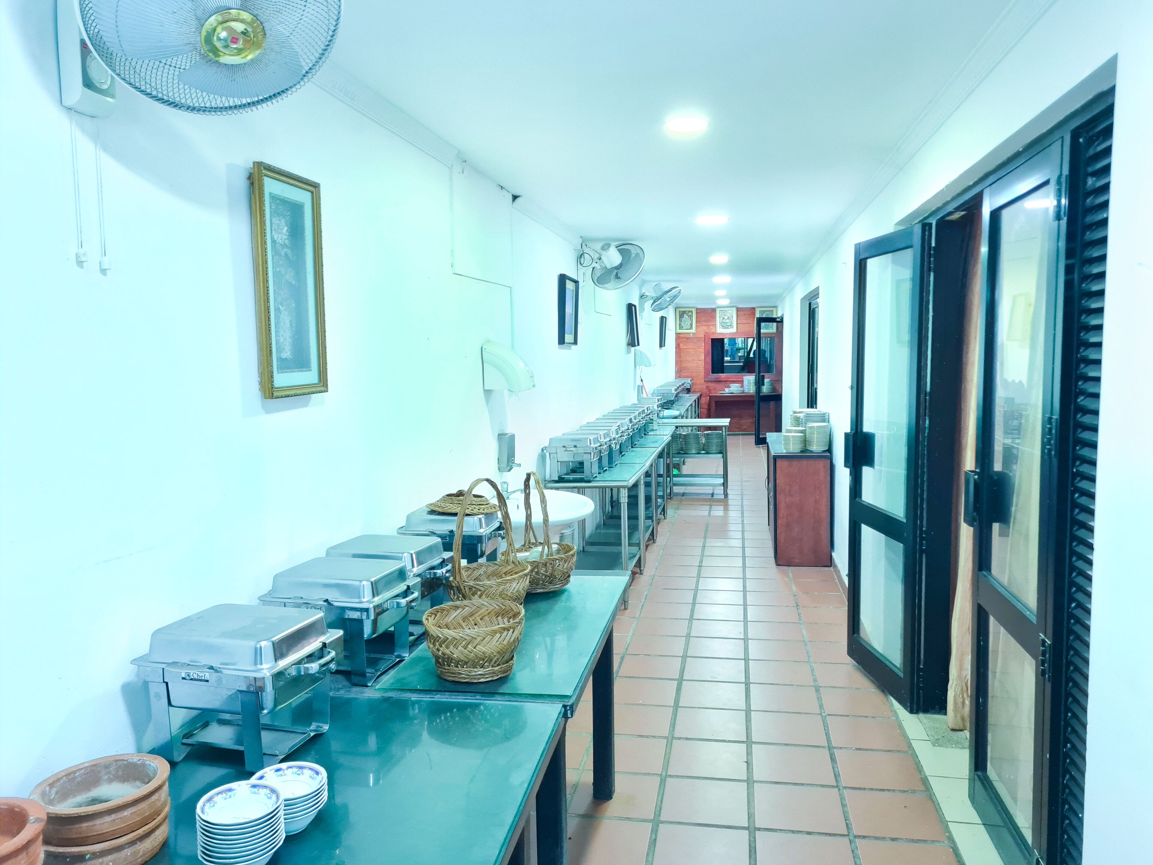 Une longue table de buffet, dotée de plusieurs présentoirs et de paniers, un sol carrelé et un ventilateur au plafond.