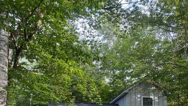 Ein zweistöckiges weißes Haus mit dunklem Dach, einer Veranda und einem kleinen Garten.