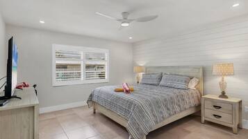 A bedroom with a bed, bedside tables, a ceiling fan, a window with blinds, and a TV on a stand.