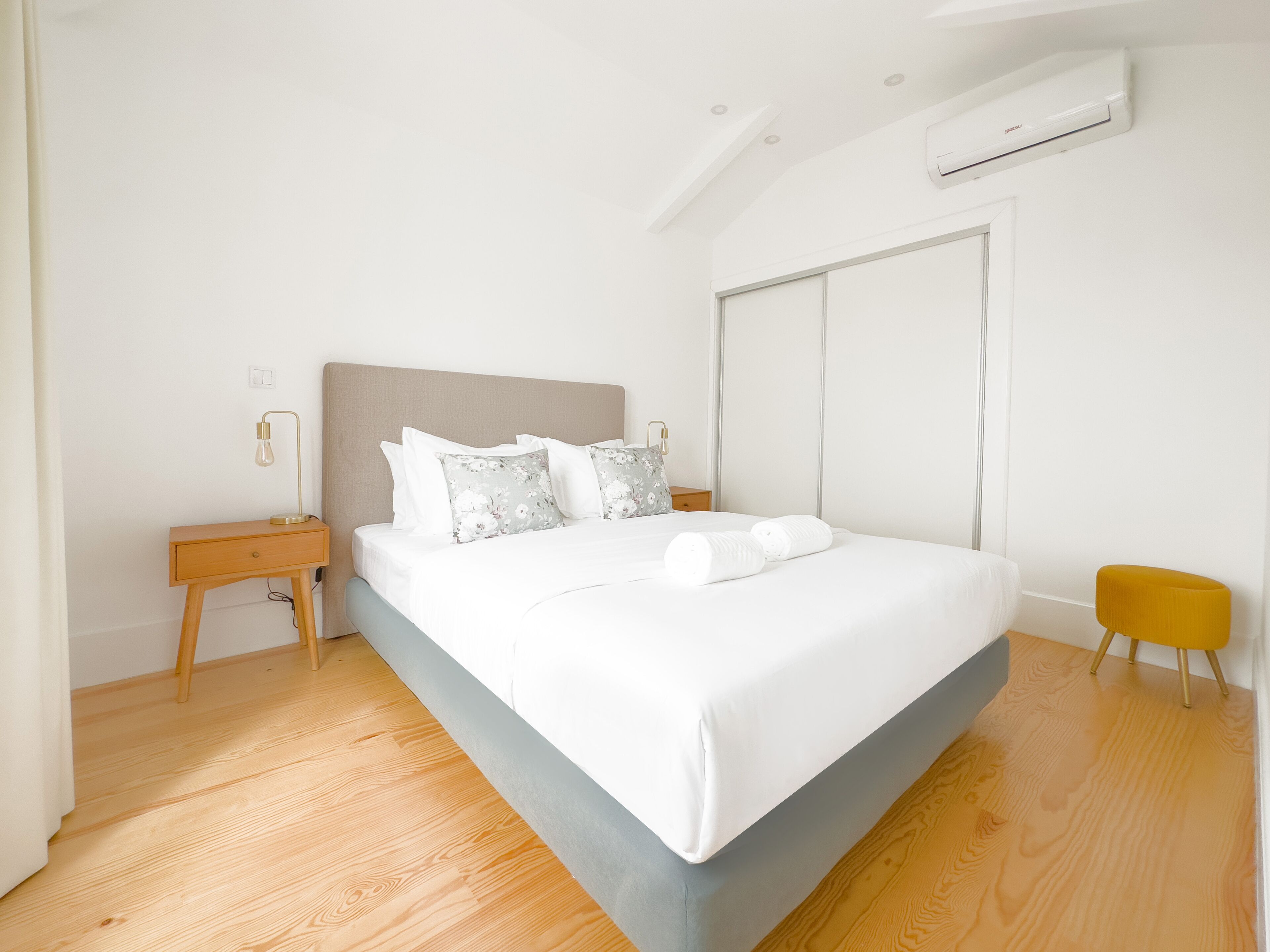 A modern bedroom with a large bed, wooden nightstands, a bedside table, and a yellow stool.