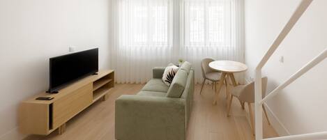 Una sala de estar moderna con un televisor de pantalla plana sobre un soporte de madera, un sofá verde, una pequeña mesa redonda y una escalera.