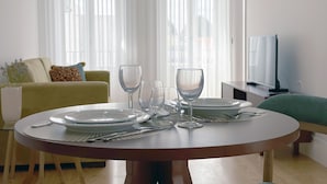 Un comedor con una mesa redonda dispuesta para cuatro personas, un sofá y un televisor al fondo.
