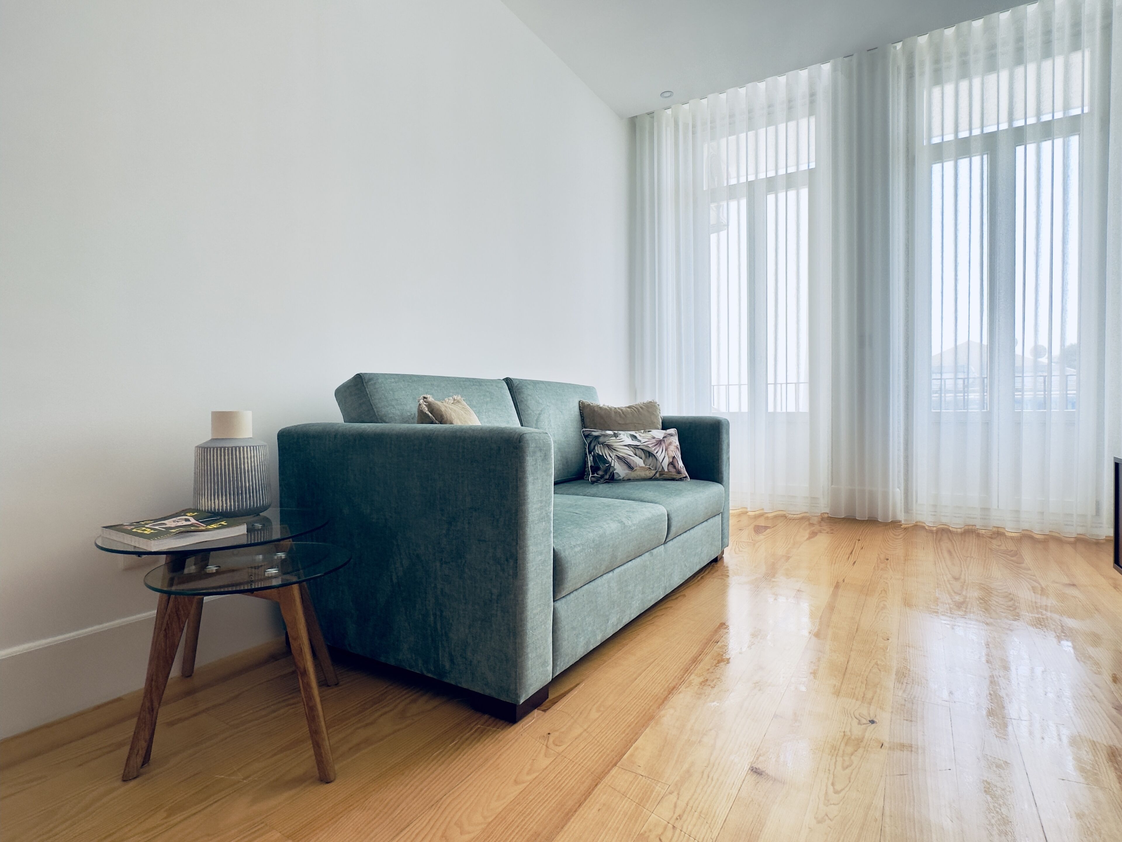 Una sala de estar con un sofá color turquesa, una mesa de centro de cristal y suelo de madera.
