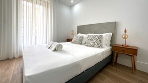 Un dormitorio moderno con una cama grande, ropa de cama blanca, almohadas estampadas, mesitas de noche de madera y una lámpara de noche.