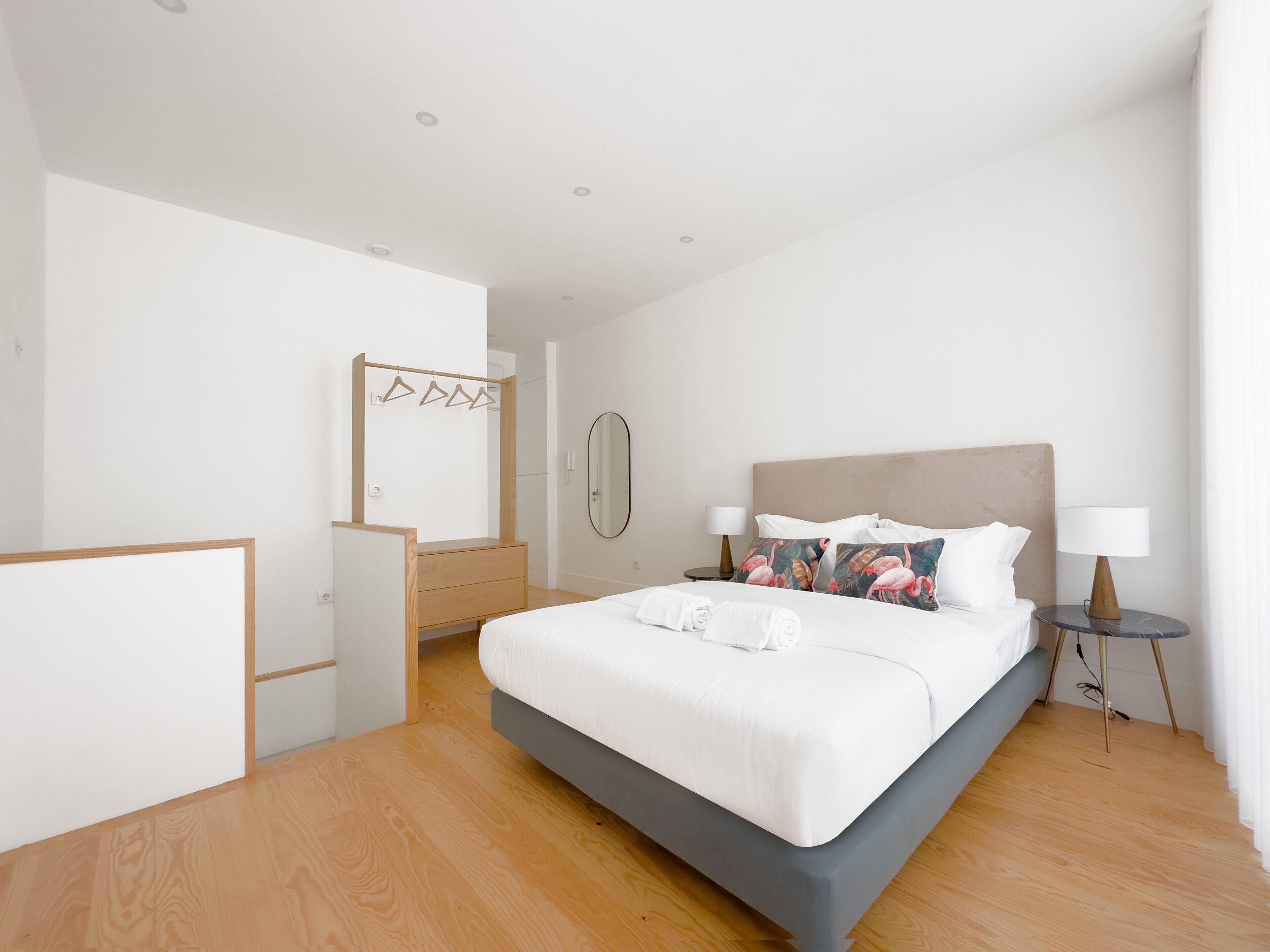 Habitación de hotel moderna con una cama grande, un aparador de madera, un espejo y una mesita de noche con lámpara.